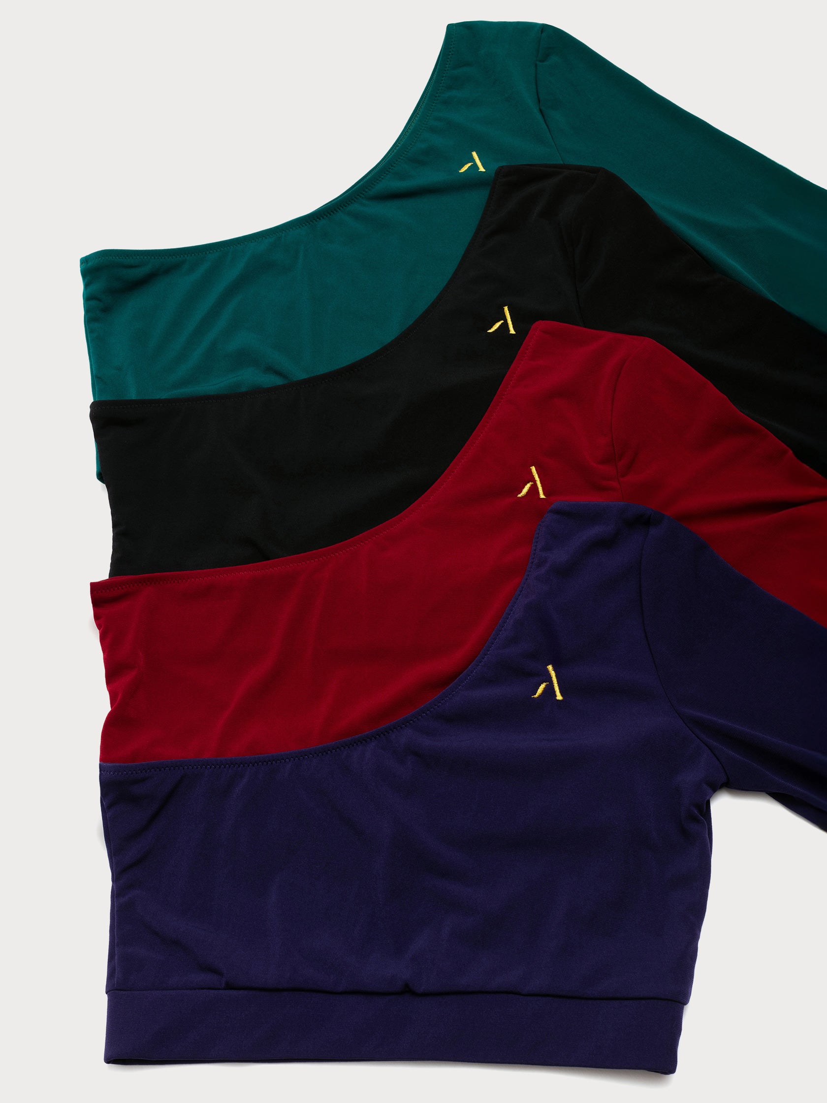 Alcuni top monospalla da pole dance in jersey colori rosso, nero, verde, viola