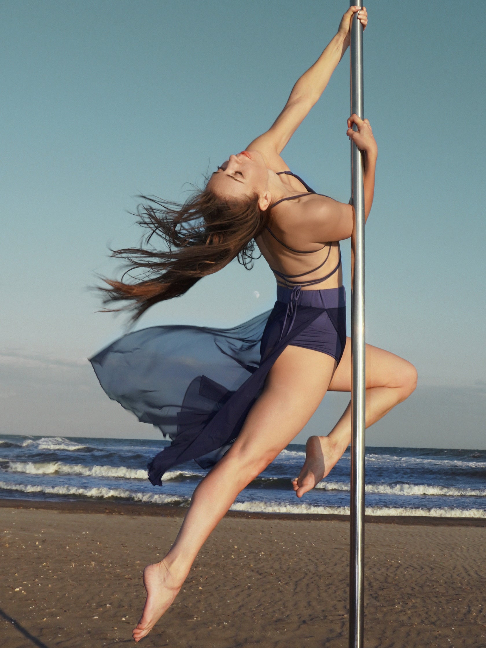 Donna sul palo in completo da pole dance blu, top a fascia e pantaloni culotte in tulle mesh