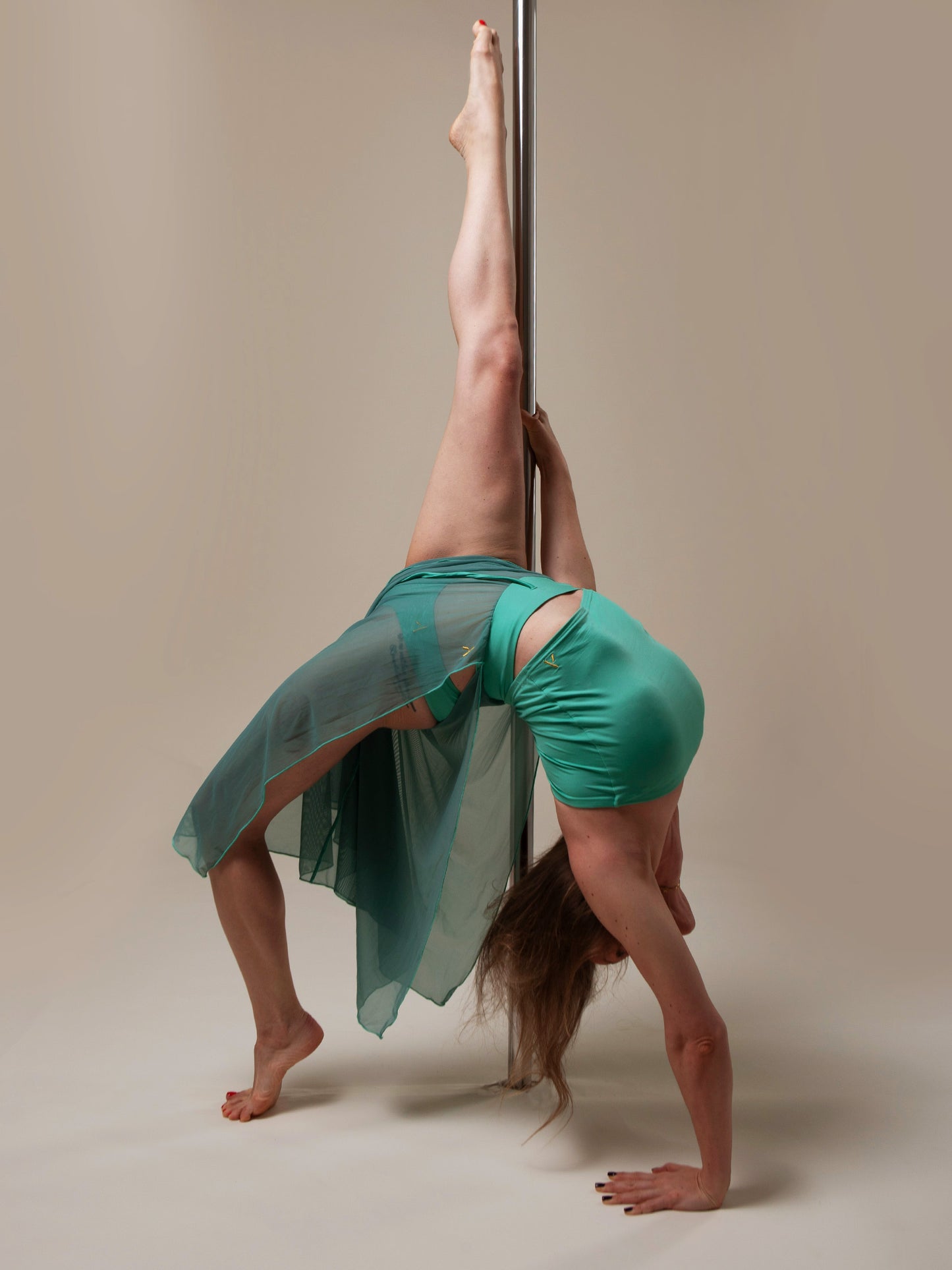 Donna sul palo in completo da pole dance verde, top a fascia e pantaloni culotte in tulle mesh