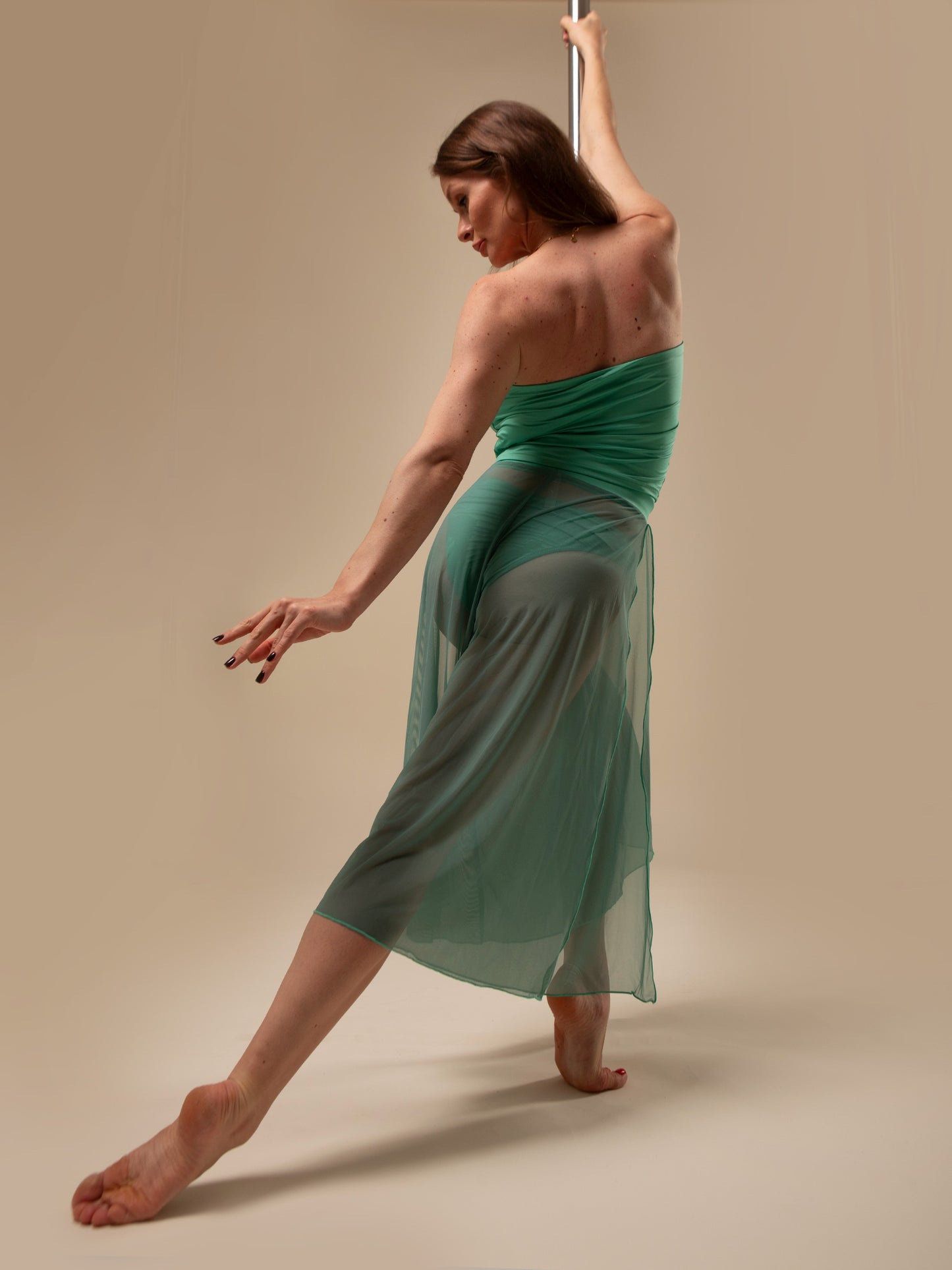 Donna sul palo in completo da pole dance verde, top a fascia e pantaloni culotte in tulle mesh